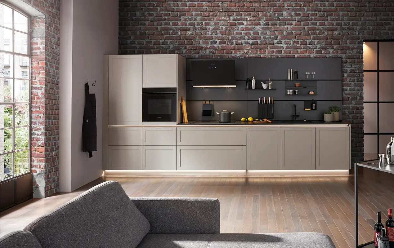 Helle Einbauküche mit Backofen, schwarzer Nischenrückwand und offenen Regalen vor roter Ziegelwand im Wohnraum.